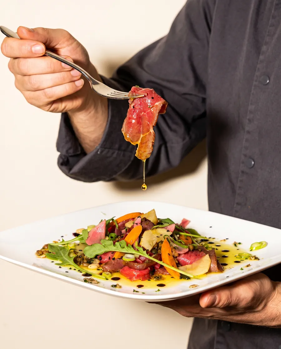 Photo du chef qui lève à la fourchette une tranche de bœuf séché maison aux épices fumées, à la Brasserie l'Échalote, la meilleure brasserie lyonnaise de Gerland, Lyon 7, quartier Jean Jaurès
